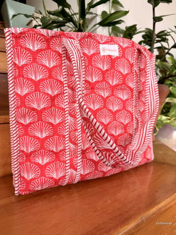 Red and white shell-patterned bag on a wooden surface with plants in the background