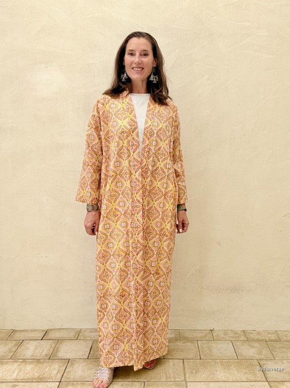 Woman wearing a long, patterned dress against a beige wall.