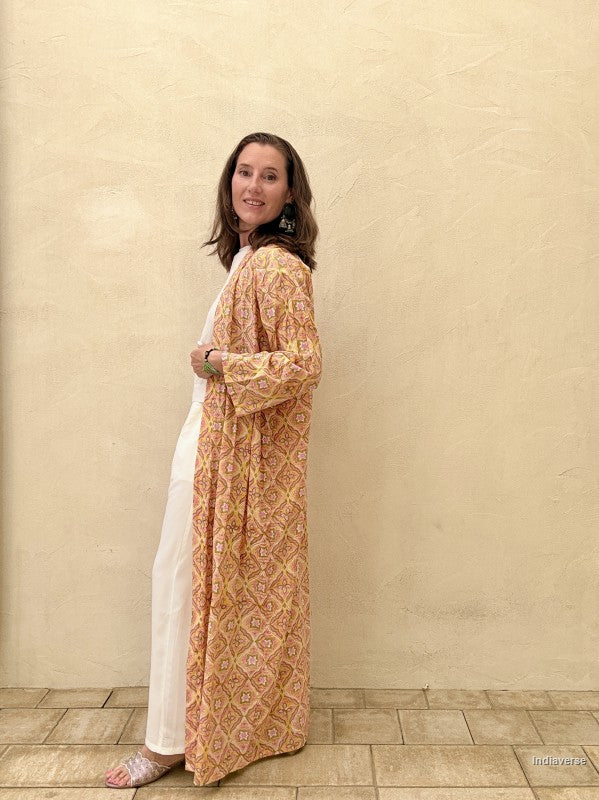 Woman wearing a patterned orange and white dress against a beige wall.