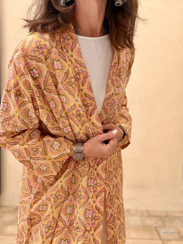 Woman wearing a patterned orange and yellow dress with a plain background