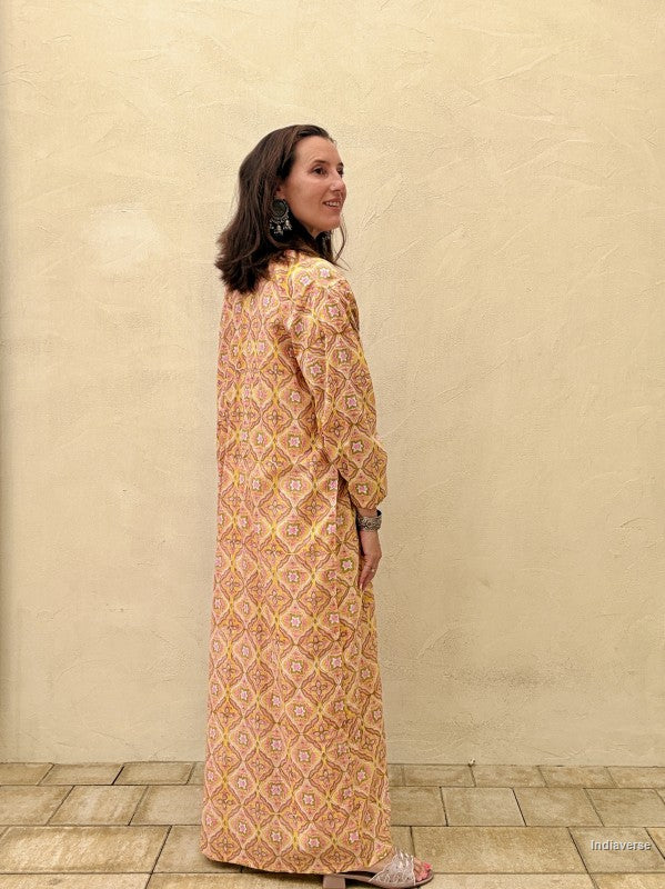Woman wearing a long, patterned dress against a beige wall.