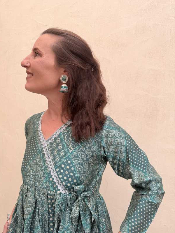 Woman wearing a green patterned dress and earrings on a beige background