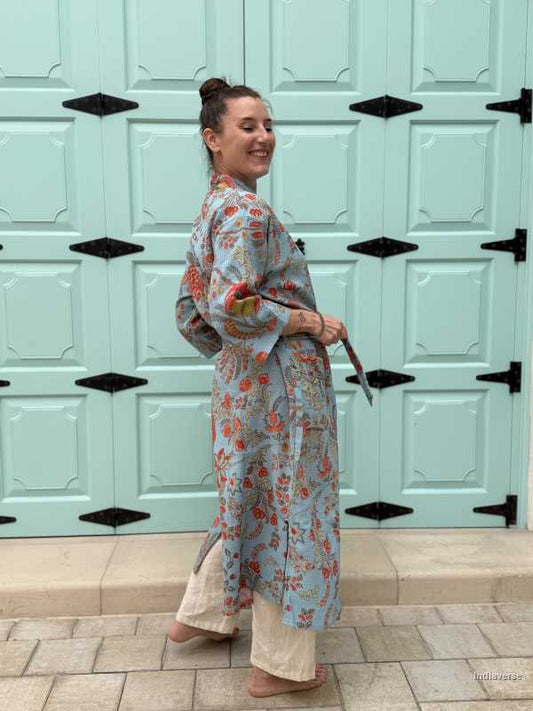  woman is wearing a blue waffle cotton bathrobe with vibrant floral print, posing in front of a pastel green paneled door