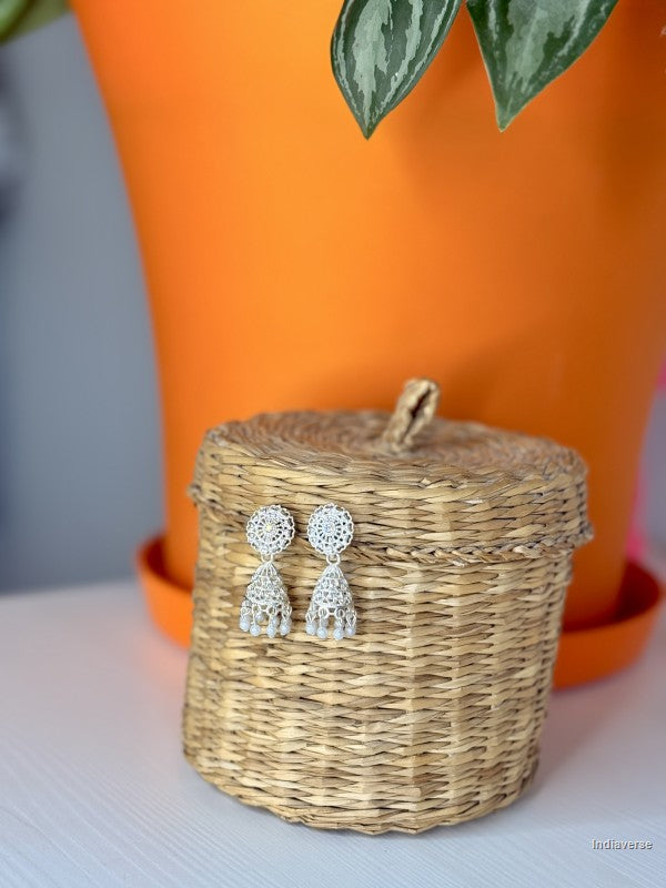 Silver earrings on a woven basket with an orange pot in the background