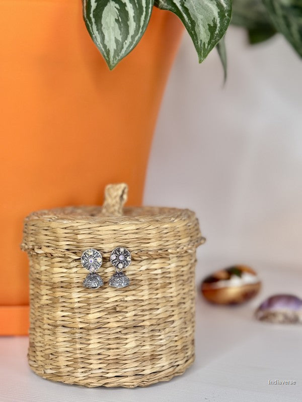 Silver earrings on a woven basket with an orange pot and plant in the background