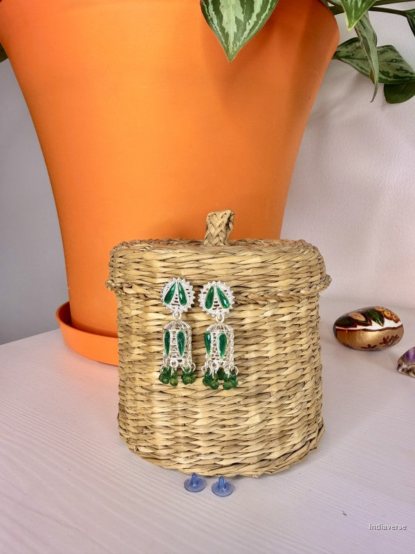 Green earrings on a woven basket with an orange pot and plant in the background