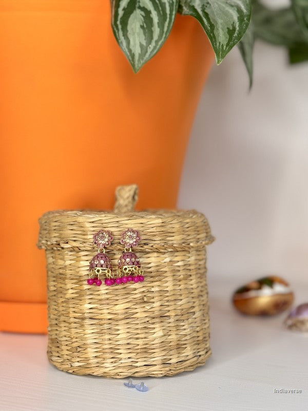 Pink earrings on a woven box with an orange pot and plant in the background