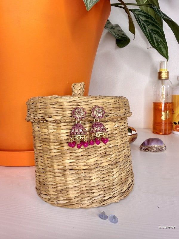 Pink beaded earrings on a woven basket with an orange pot and plant in the background.