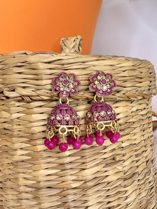 Pink and gold earrings on a woven basket with an orange and white background