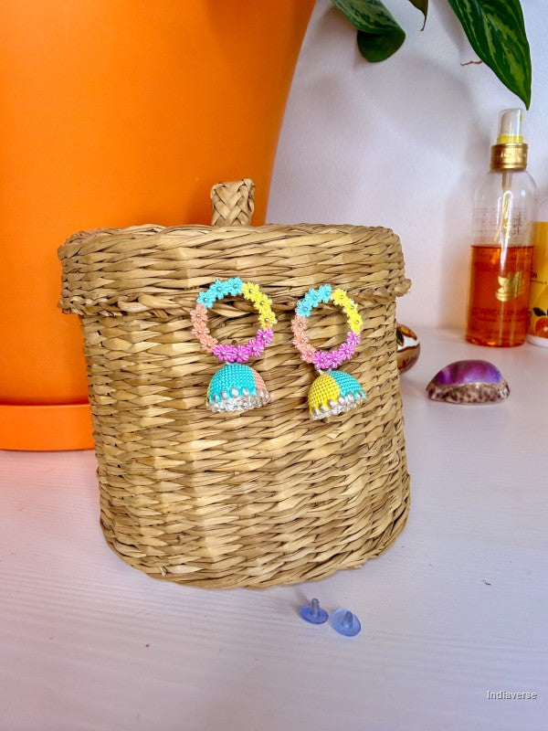 Colorful earrings on a woven basket with a plant and bottle in the background