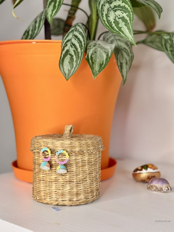 Colorful earrings on a woven basket with an orange pot and plant in the background