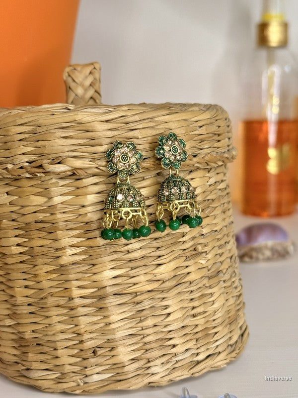 Gold and green earrings on a woven basket with a blurred background