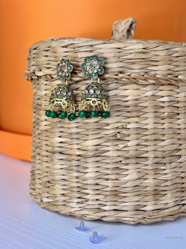 Pair of green and gold earrings on a woven basket with an orange background