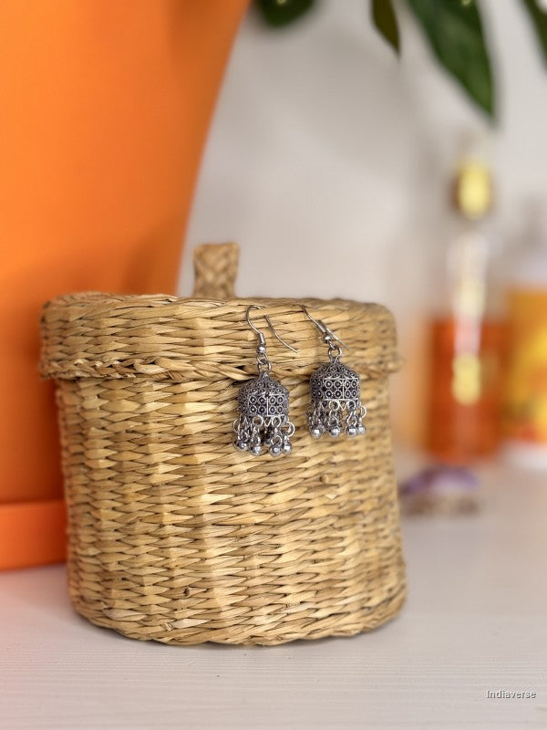Silver bell-shaped earrings on a woven basket with a blurred background