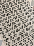 A close-up of a woven rug or textile with a repeating black geometric chevron pattern on a warm off-white background.
