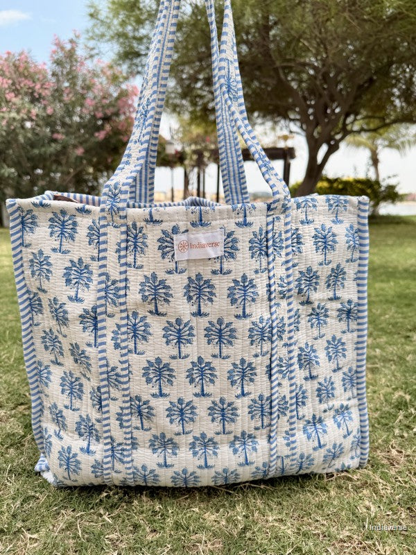 Blue and white patterned tote bag with a brand label on grass
