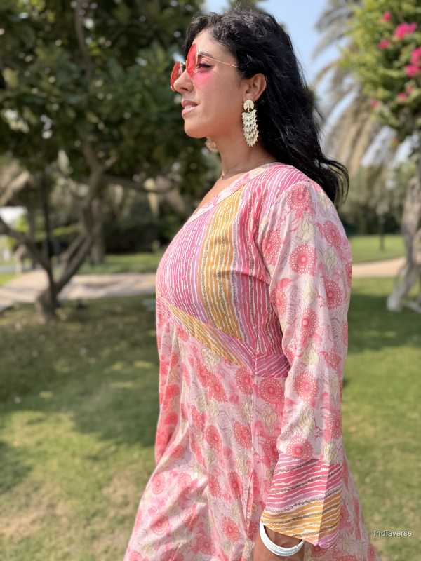 Woman wearing a pink and yellow floral dress outdoors with greenery in the background