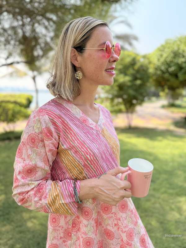 Woman in a pink floral dress holding a pink mug outdoors with trees and grass in the background