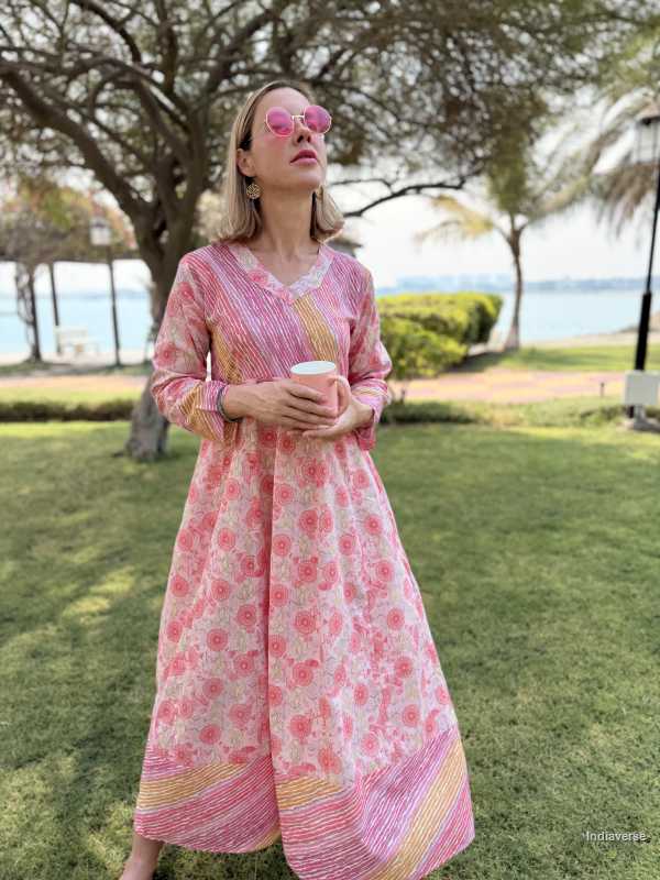 Woman in a pink floral dress standing outdoors with trees and water in the background