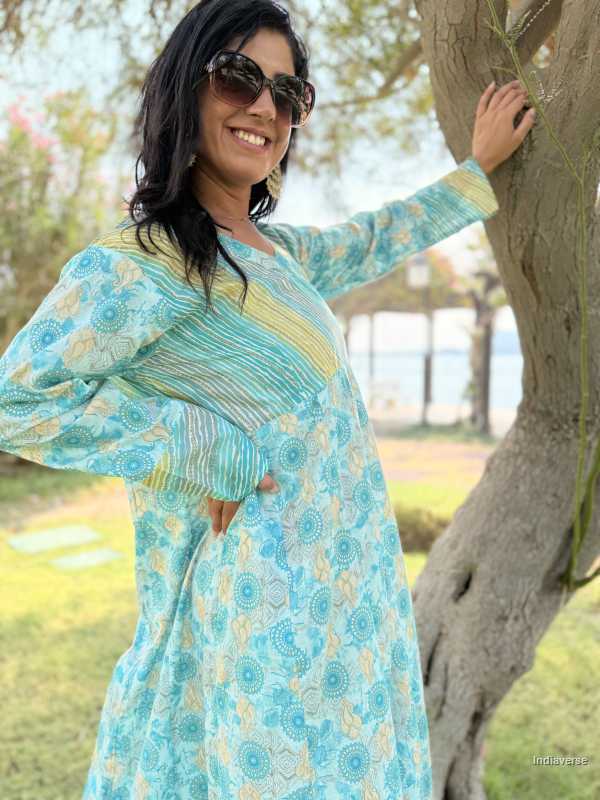 Woman in a blue floral dress standing next to a tree outdoors