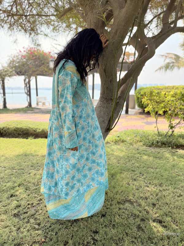 Person wearing a blue and green patterned dress standing under a tree with a scenic background.