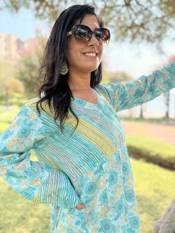 Woman wearing a blue and green patterned outfit with sunglasses outdoors.