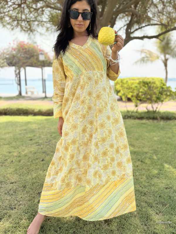 Woman in a yellow floral dress standing outdoors with greenery and trees in the background