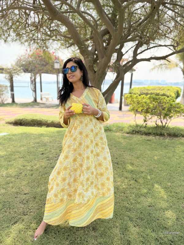 Woman in a yellow dress standing in a park with trees and grass.