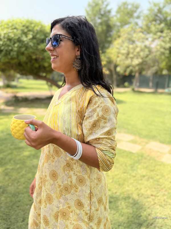 Woman in a yellow floral dress holding a cup outdoors