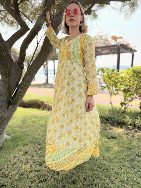 Woman in a yellow floral dress standing outdoors near a tree