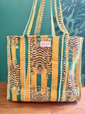 Tote bag with tiger pattern on a wooden surface against a green wall with leaf design.