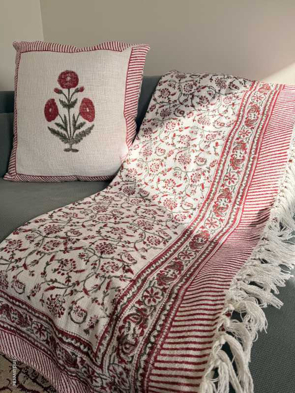 Decorative red and white patterned throw blanket with fringe on a surface, accompanied by a matching pillow.