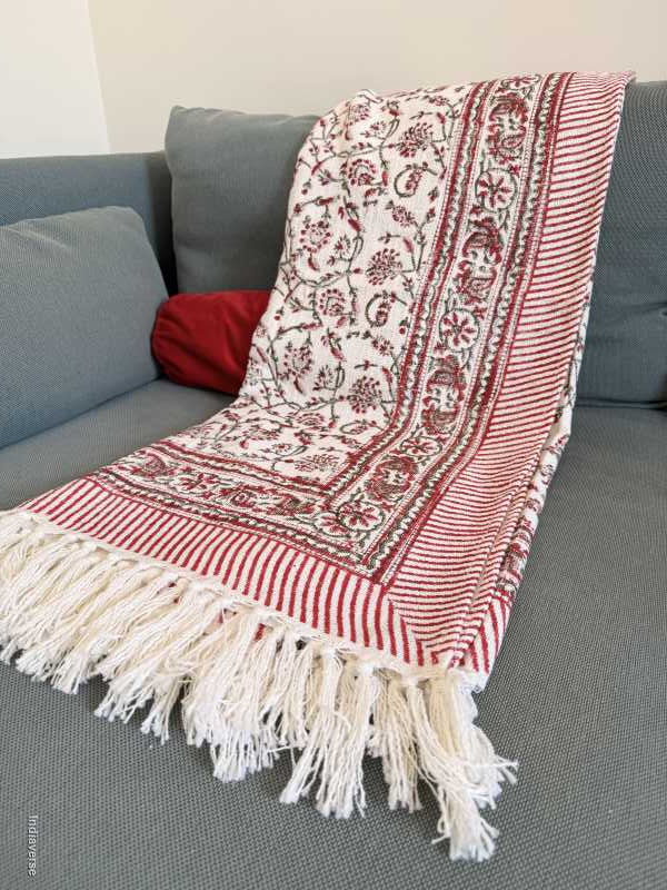 Red and white patterned throw with fringes draped over a gray couch