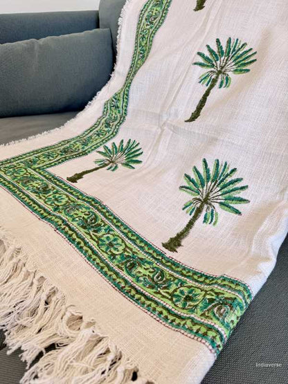 Embroidered blanket with palm tree designs on a gray couch.