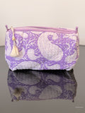 purple toiletry bag with tassel sitting on a glass surface