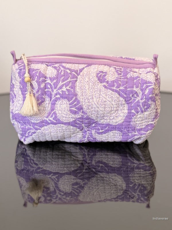 purple toiletry bag with tassel sitting on a glass surface