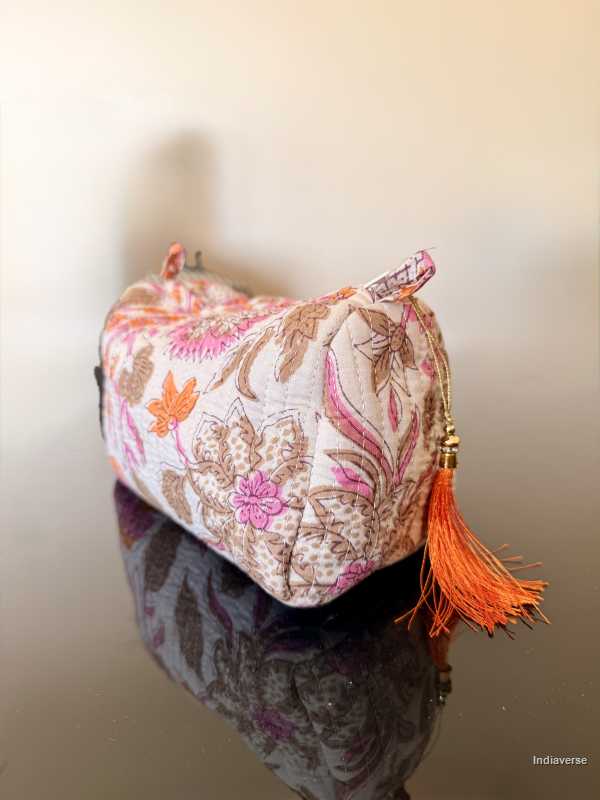 Decorative pouch with floral pattern and orange tassel on a reflective surface. | Paradise