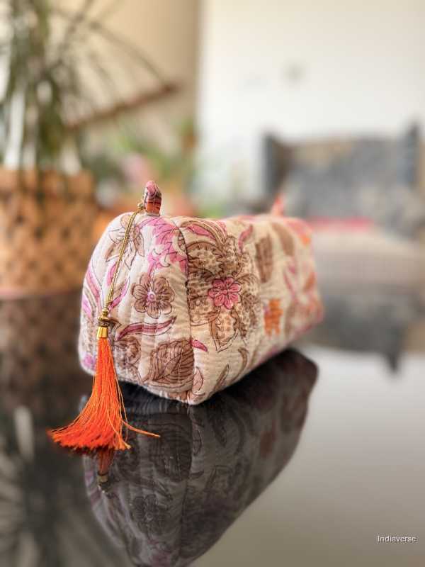 Decorative cylindrical pillow with floral pattern and orange tassel on a reflective surface. | Paradise