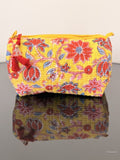 yellow floral toiletry bag with red tassels sitting on a glass surface