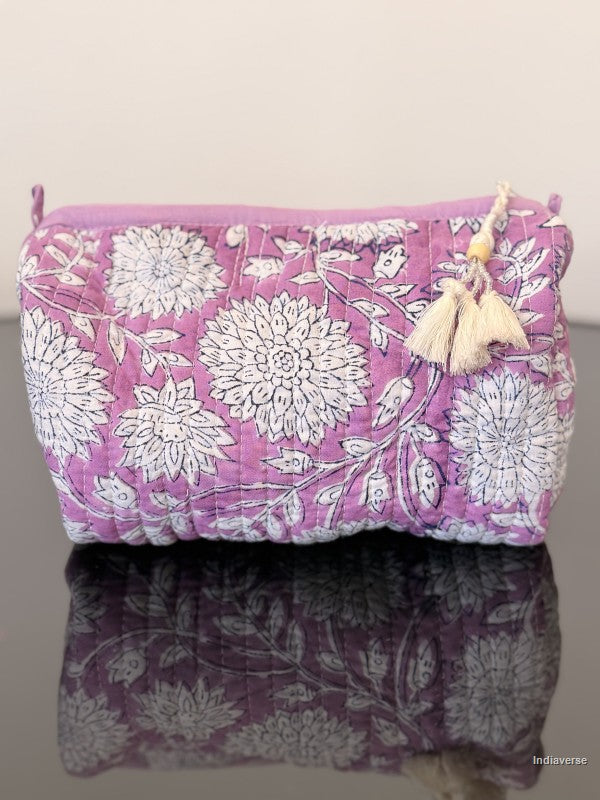purple toiletry bag with white tassels sitting on a glass surface