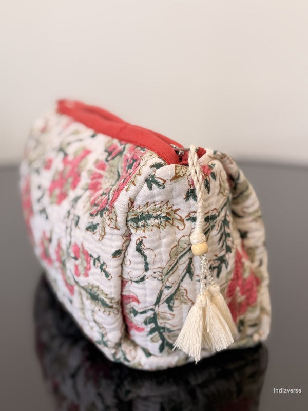 Floral patterned pouch with a red top and tassel on a reflective surface.