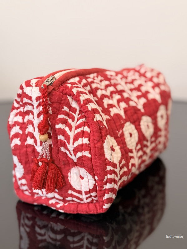 red toiletry bag with a tassel and white flowers sitting on a glass surface