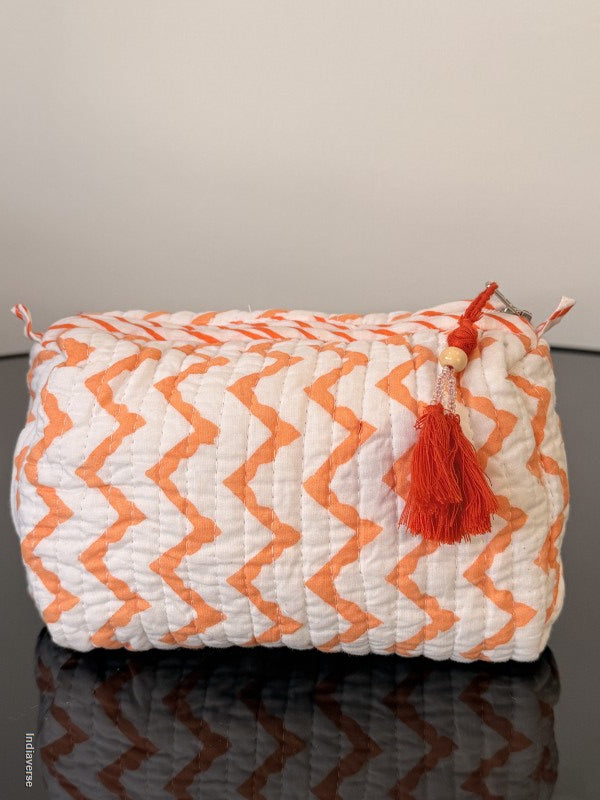small toiletry bag with orange zig-zag pattern sitting on a glass surface
