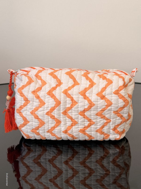 Orange and white zigzag patterned pillow with tassel on a plain background