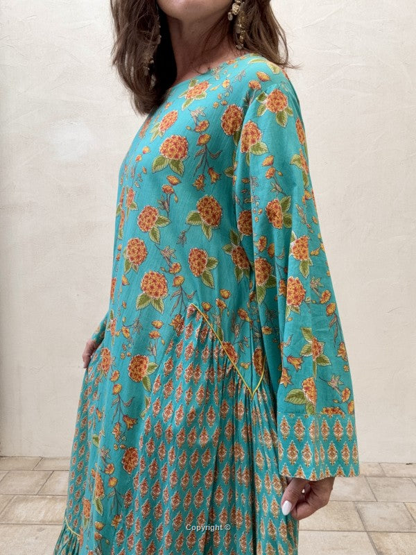 Woman wearing a teal floral dress against a white wall.