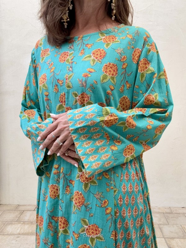 Person wearing a turquoise dress with orange floral pattern indoors.