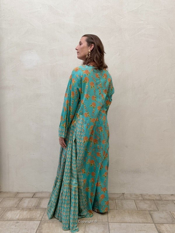 Woman wearing a teal floral dress standing against a plain wall.