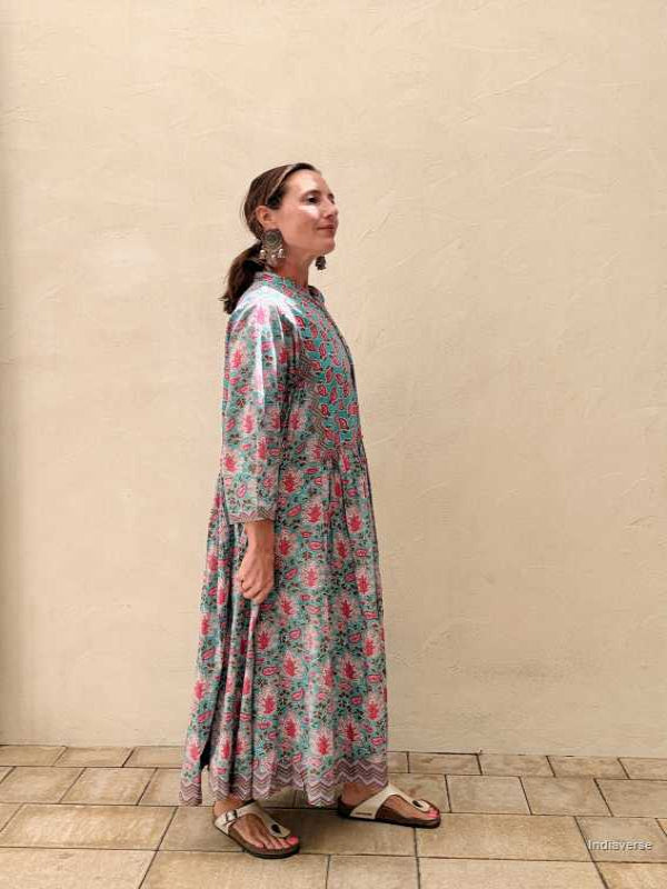 Woman wearing a midi size cotton dress with floral print standing in front of a beige wall