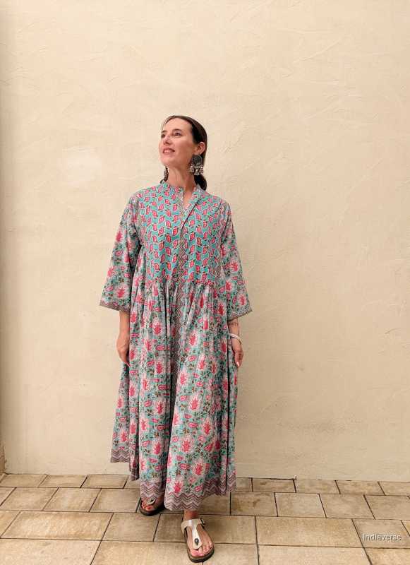 Woman wearing a midi size cotton dress with floral print standing in front of a beige wall