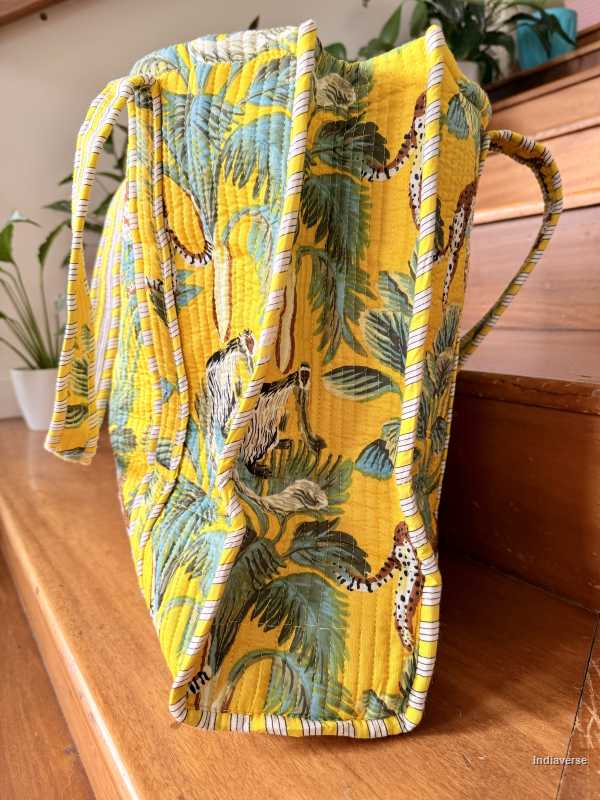 Yellow quilted tote bag with animal and leaf pattern on a wooden surface